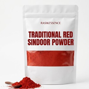 Puede incluir: Una bolsa blanca vertical que contiene polvo de sindoor rojo con el texto RASIKESSENCE y TRADITIONAL RED SINDOOR POWDER impreso en el frente. Una pequeña cuchara de madera descansa junto a un montón de polvo rojo vibrante frente a la bolsa.