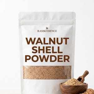 Könnte beinhalten: Ein weißer Standbeutel mit der Aufschrift RASIKESSENCE WALNUT SHELL POWDER in brauner Schrift. Der untere Teil des Beutels ist transparent und zeigt das hellbraune, körnige Pulver. Eine kleine Holzschaufel liegt in einer Holzschale mit Pulver.