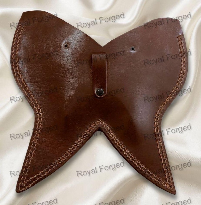 Op de afbeelding: Een bruine leren gorget in vlindervorm, met lichtbruine gestikte randen. Het heeft een kleine riem met een knoop. De achtergrond toont de tekst "Royal Forged".