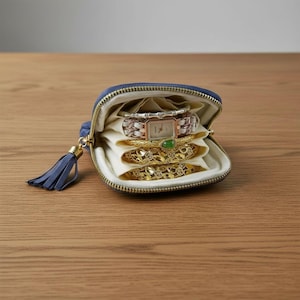 Può includere: Un portagioie con cerniera blu navy con un nappa, aperto per rivelare un orologio e diversi braccialetti d'oro. La custodia è foderata in tessuto color crema e i braccialetti sono impilati all'interno.