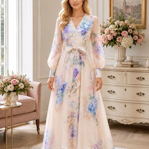Puede incluir: Un vestido largo de manga larga en color crema claro con un estampado floral vibrante en tonos azules, morados y verdes. El vestido tiene un escote en V, una parte delantera abotonada con peque&ntilde;os botones redondos y un cintur&oacute;n de tela a juego.
