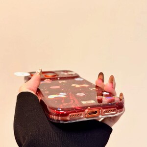 Puede incluir: Una funda de tel&eacute;fono roja transparente con un dise&ntilde;o brillante que presenta nubes, estrellas y la Torre Eiffel. La funda tiene un parachoques protector y recortes para las funciones del tel&eacute;fono.