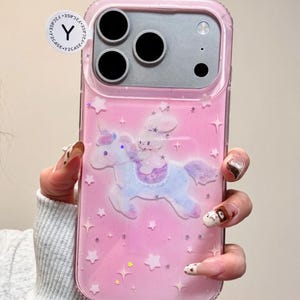 May include: Pink phone case with a unicorn and bunny design. The case has a clear border and features a unicorn with a bunny rider, surrounded by stars. The case is designed for a smartphone with three camera lenses.