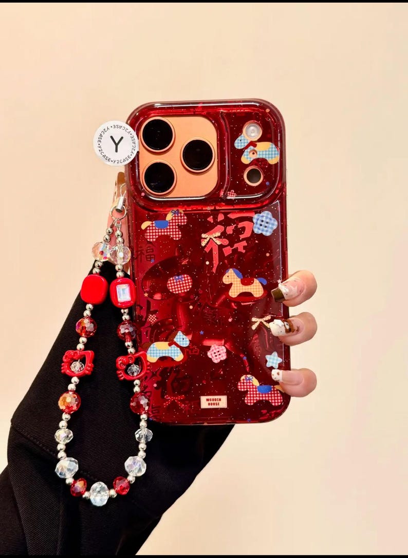Puede incluir: Funda de tel&eacute;fono roja con un dise&ntilde;o decorativo con caballos, nubes y estrellas. La funda tiene una correa de mu&ntilde;eca a juego con cuentas rojas y transparentes. La funda tiene un acabado transparente y brillante.