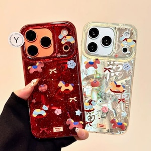 Puede incluir: Dos fundas de tel&eacute;fono con dise&ntilde;os decorativos. Una es de color rojo intenso con acabado brillante, con motivos de caballitos de juguete y lazos. La otra es transparente con dise&ntilde;os similares. Ambas fundas tienen un recorte para cuatro lentes.