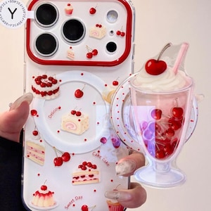May include: Clear phone case with a red border and a cherry and cake design. The case features images of cherries, cupcakes, and cake slices. A 3D cherry milkshake is attached to the case.