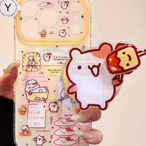 May include: A clear phone case with a yellow border and a cartoon design. The case features illustrations of cute characters, food, and text. A clear, heart-shaped charm with a cartoon bear holding a popsicle is attached to the case.