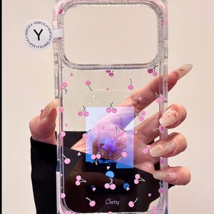 May include: Clear phone case with a pink cherry pattern. The case has a transparent design with small pink cherry illustrations scattered across the surface. The word "Cherry" is printed at the bottom.