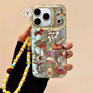 Puede incluir: Funda de tel&eacute;fono transparente con un dise&ntilde;o decorativo con ilustraciones de caballos balanc&iacute;n rojos, azules y blancos y caracteres chinos. La funda tiene una correa de mu&ntilde;eca de cuentas amarillas y blancas.