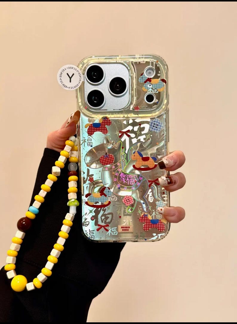Puede incluir: Funda de tel&eacute;fono transparente con un dise&ntilde;o decorativo con ilustraciones de caballos balanc&iacute;n rojos, azules y blancos y caracteres chinos. La funda tiene una correa de mu&ntilde;eca de cuentas amarillas y blancas.