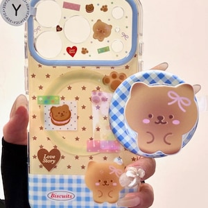 May include: Clear phone case with a blue border and a yellow background decorated with star and bear-themed stickers. A matching bear-shaped phone grip is attached. The case has the text "Love Story" and "Biscuits".