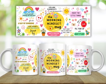 May include: A white ceramic mug featuring a colorful, busy graphic design with yellow suns, rainbows, flowers, and a cat. The text reads: THE MORNING MINDSET MUG, YOU ARE PURRRFECT, DREAM BIG, ENJOY THE LITTLE THINGS, and FILL YOUR CUP WITH GRATITUDE.