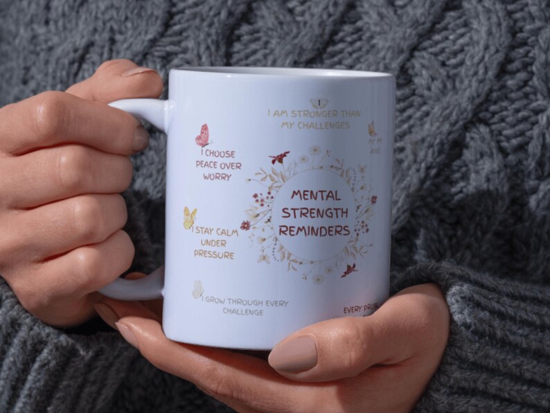 May include: White ceramic mug with the text "Mental Strength Reminders" surrounded by floral and butterfly illustrations. Additional phrases include "I choose peace over worry" and "Stay calm under pressure."
