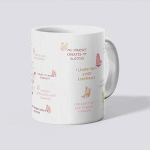 May include: White ceramic mug with a handle, featuring inspirational text and watercolor butterfly illustrations in shades of pink and peach. The mug has phrases like "My Mindset Creates My Success" and "I Trust My Inner Strength."