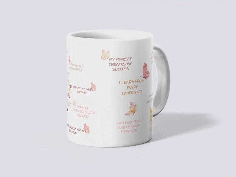May include: White ceramic mug with a handle, featuring inspirational text and watercolor butterfly illustrations in shades of pink and peach. The mug has phrases like "My Mindset Creates My Success" and "I Trust My Inner Strength."