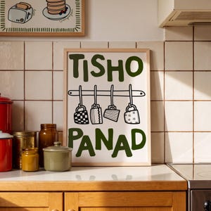 May include: A rectangular framed wall art print featuring the dark green text TISHO at the top and PANAD at the bottom. Between the words is a black line drawing of a kitchen rack with four hanging mugs, each with a unique pattern.