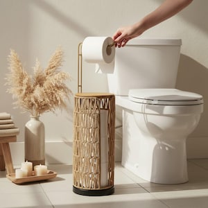 May include: A woven toilet paper holder with a wooden top and black base. A gold-colored toilet paper holder is attached to the top. A white toilet is in the background. A hand is reaching for the toilet paper.