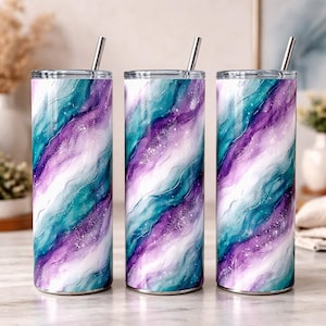 May include: Three stainless steel tumblers with lids and straws. The tumblers feature a swirling design in shades of teal, purple, and white, with a galaxy-like effect. The design covers the entire surface of the tumblers.