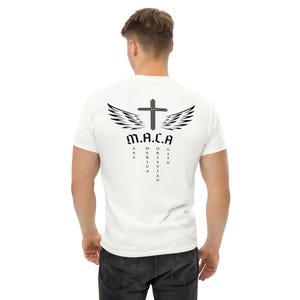May include: White t-shirt with a black graphic design on the back. The design includes a cross, wings, and the acronym "M.A.C.A." with the words "Make America Christian Again" vertically aligned. The shirt is a casual, short-sleeved style.