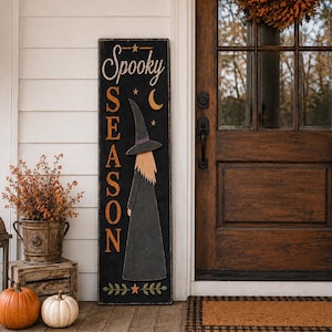Op de afbeelding: Een hoog rechthoekig zwart houten bord met de tekst Spooky Season in witte en oranje letters. Het ontwerp bevat een uitgesneden heks met een puntmuts, een maansikkel, kleine sterren en een groene bladrand aan de onderkant.