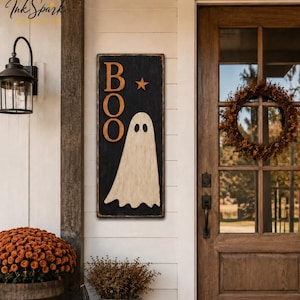 Puede incluir: Un letrero de pared vertical rectangular con fondo negro que presenta el texto naranja BOO, una pequeña estrella naranja y una gran figura de fantasma blanco. El letrero tiene un acabado desgastado y está montado en una pared blanca.