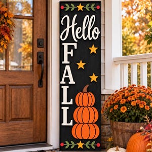 Könnte beinhalten: Ein hohes, rechteckiges schwarzes Holzschild mit dem weißen Schriftzug "Hello" über den vertikalen weißen Buchstaben "FALL". Das Design zeigt drei gestapelte orangefarbene Kürbisse, gelbe Sterne sowie grüne Blattmotive an den Rändern.