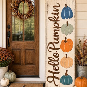 Puede incluir: Un letrero de porche rectangular y alto de madera con un acabado blanco desgastado. El letrero presenta el texto marrón oscuro "Hello Pumpkin" escrito verticalmente, acompañado de cinco calabazas de madera pintadas y apiladas en azul, salvia, naranja, melocotón y verde azulado.