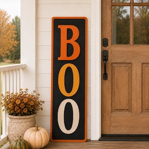 Puede incluir: Un letrero vertical negro, alto y rectangular, que presenta la palabra BOO en letras grandes, apiladas y tridimensionales. La letra B es naranja, la primera O es amarillo dorado y la segunda O es crema, sobre un fondo negro.