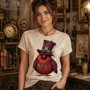 May include: Beige t-shirt featuring a red cardinal bird wearing a steampunk top hat adorned with gears and clocks. The bird has a matching necklace and is set against a vintage background. The shirt has rolled-up sleeves and a crew neck.