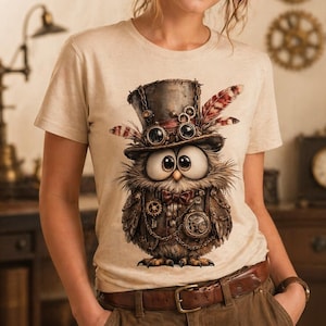May include: Beige t-shirt featuring a whimsical steampunk owl design. The owl is adorned with goggles, a top hat, and gears, with a red bow tie and feathers. The shirt has the text "Ink Spark Creative" at the top.