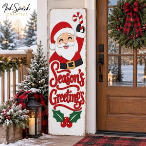 May include: A tall rectangular white wooden porch sign featuring a smiling Santa Claus holding a red and white candy cane, with the red text Season's Greetings and a green holly and red berry graphic at the bottom, displayed on a porch.