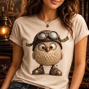 May include: Beige t-shirt featuring a whimsical owl character wearing a steampunk-style aviator helmet with goggles. The owl has large eyes and mechanical-looking boots. The shirt has the text "Ink Spark Creative" at the top.