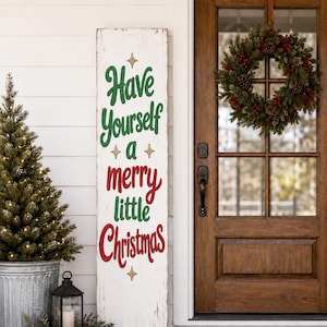 Könnte beinhalten: Ein hohes, rechteckiges weißes Holzschild mit abgenutzter Oberfläche, das den grün-roten Schriftzug Have Yourself a merry little Christmas trägt, akzentuiert durch kleine goldene Sternsymbole, vertikal neben einer hölzernen Eingangstür.