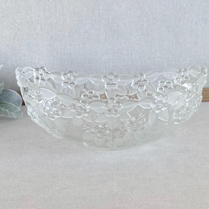May include: A clear glass bowl featuring a raised, frosted floral pattern across its entire exterior surface. The design consists of repeating flower blossoms and leaves, creating a textured, semi-opaque appearance against the transparent glass.