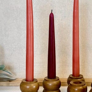 May include: A collection of wooden candle holders with red and burgundy taper candles. The candle holders are made of turned wood and have a classic, rounded design. The candles are of varying heights, creating a visually interesting display.