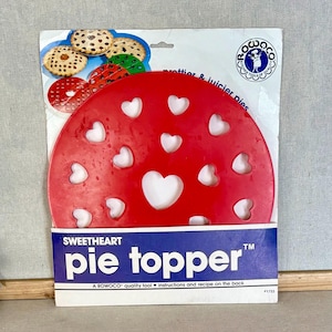 May include: A red circular plastic pie topper featuring multiple heart-shaped cutouts, packaged on a white and blue cardboard backing labeled Sweetheart pie topper with the Rowoco logo and text describing it for prettier and juicier pies.