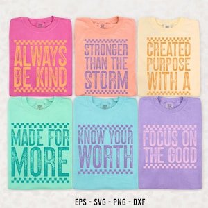 May include: Six colorful t-shirts with inspirational quotes. The shirts are pink, peach, yellow, mint green, light blue, and purple. The quotes include "Always Be Kind," "Stronger Than The Storm," and "Focus On The Good."