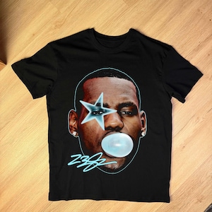 May include: Black t-shirt featuring a graphic of a person with a star over one eye and a bubble of gum. The graphic is outlined in blue, with the number "23" in a stylized font below the face.