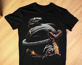 Puede incluir: Camiseta negra con un diseño de baloncesto. Una serpiente está envuelta alrededor de la pelota, con un jugador de baloncesto y una firma en blanco. La camiseta está hecha de un material suave.