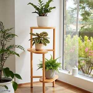 May include: A three-tiered wooden plant stand with three potted plants. The stand has a natural wood finish and holds a variety of green plants in white and gray pots. The stand is positioned near a window with a view of greenery.