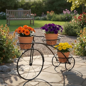 May include: A black metal bicycle-shaped plant stand with three terracotta pots filled with colourful flowers. The flowers are orange, purple, and yellow. The stand is on a stone patio in a garden setting.