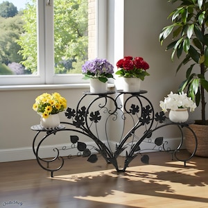 May include: A black metal plant stand with four tiers, each holding a white pot with colorful flowers. The stand has a decorative vine and leaf design. The flowers include yellow, purple, red, and white blooms.