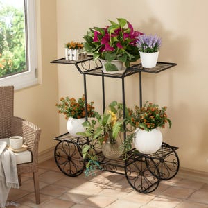 Può includere: Un portapiante in metallo nero a tre livelli, simile a un carrello con ruote a raggi. Espone varie piante in vaso con vivaci foglie viola, arancioni e verdi. È visibile anche un piccolo vaso bianco in stile staccionata.