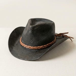 May include: A distressed black cowboy hat with a brown leather band and decorative ties. The hat has a wide brim and a classic western design. The hat is a stylish accessory.
