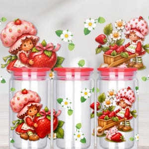 May include: Three clear glass cylindrical jars with red lids, each featuring a printed design of a character wearing a strawberry-patterned hat, holding large red strawberries, and accompanied by white strawberry blossoms and green leaves.