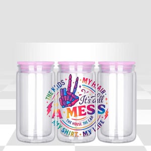 May include: Three clear glass jars with pink lids. The center jar has a colorful graphic that reads "It's all a MESS" with the words "The Kids, My Hair, My Shirt, My Life, The House, The Car" surrounding the text. The graphic includes a peace sign.