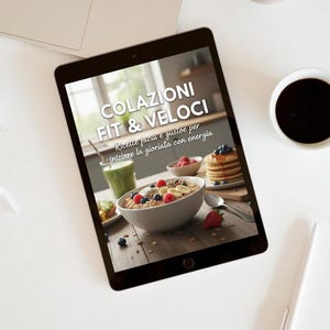 Può includere: Un tablet mostra un'immagine di colazione sana con il testo "COLAZIONI FIT & VELOCI" e "Ricette facili e gustose per iniziare la giornata con energia." Un laptop, una tazza di caffè e una penna sono su una superficie bianca.