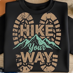 May include: Black sweatshirt with a graphic design featuring the words "HIKE Your WAY" in a distressed font, with a mountain range illustration. The design is in shades of brown and teal.