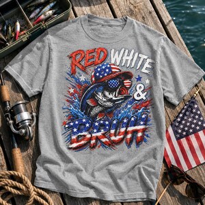 Op de afbeelding: Een grijs gemêleerd T-shirt met een afbeelding van een vis die een zonnebril en een baseballpet met het Amerikaanse vlagpatroon draagt. De tekst luidt RED WHITE & BRUH, met letters in de patriottische kleuren rood, wit en blauw.
