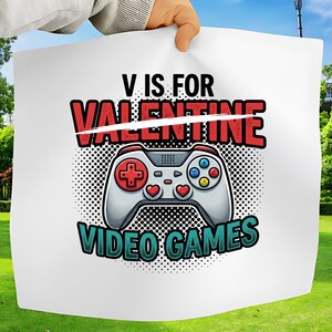 Könnte beinhalten: Weißes Grafikdesign mit einem Videospiel-Controller mit roten Akzenten und dem Text "V IS FOR VALENTINE VIDEO GAMES". Das Design hat einen gepunkteten Hintergrund und wird von einer Person gehalten.